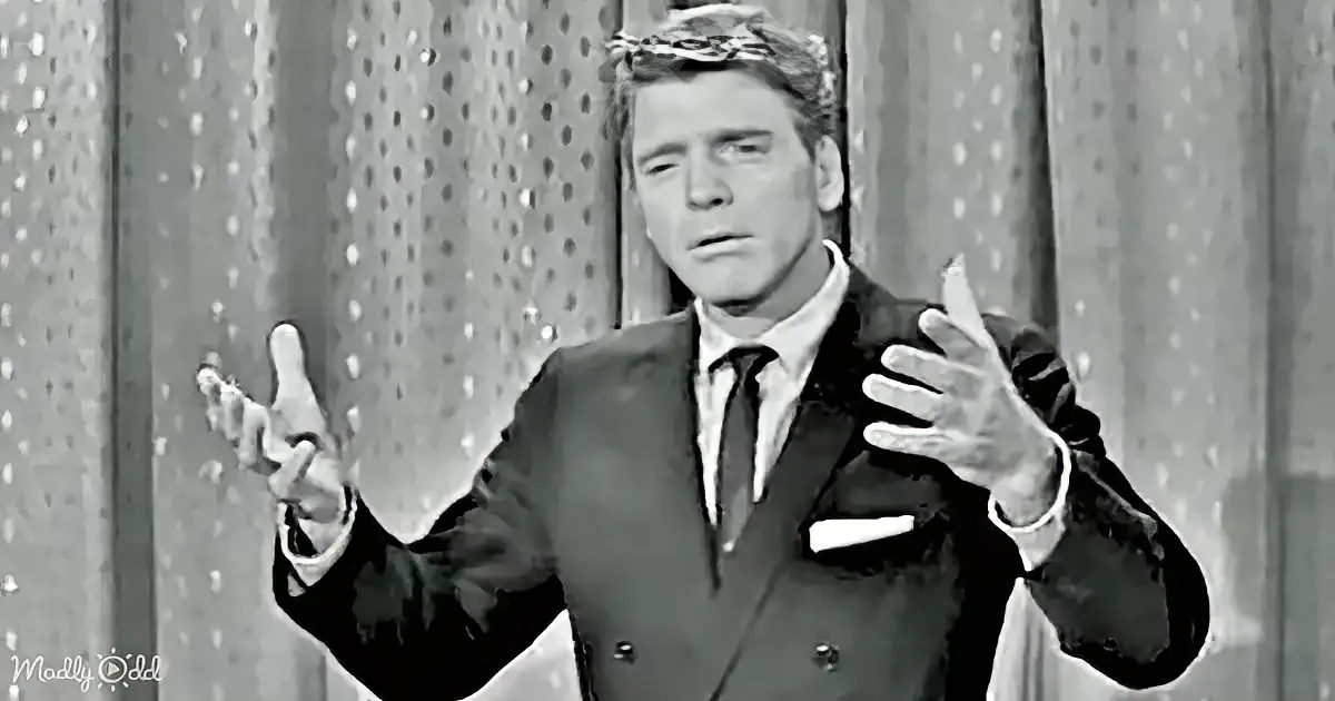 A man in a suit gestures dramatically, wearing a crown, against a polka-dot backdrop.