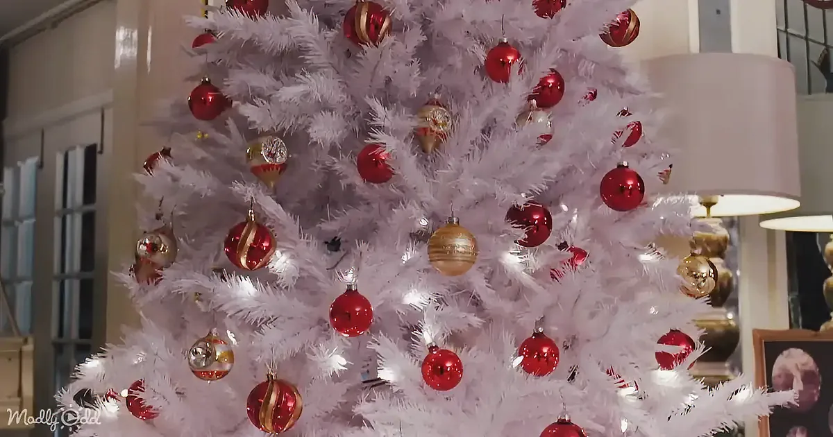A white Christmas tree adorned with red and gold ornaments stands in a cozy room.