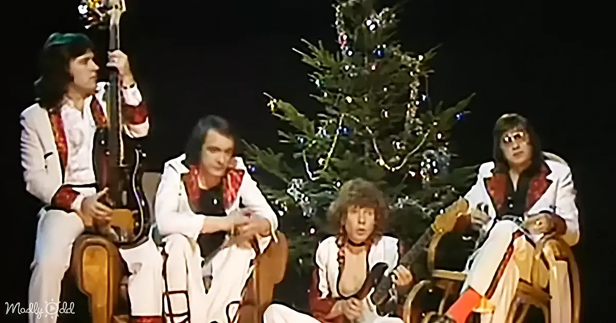 A band in white suits plays instruments in front of a decorated Christmas tree.