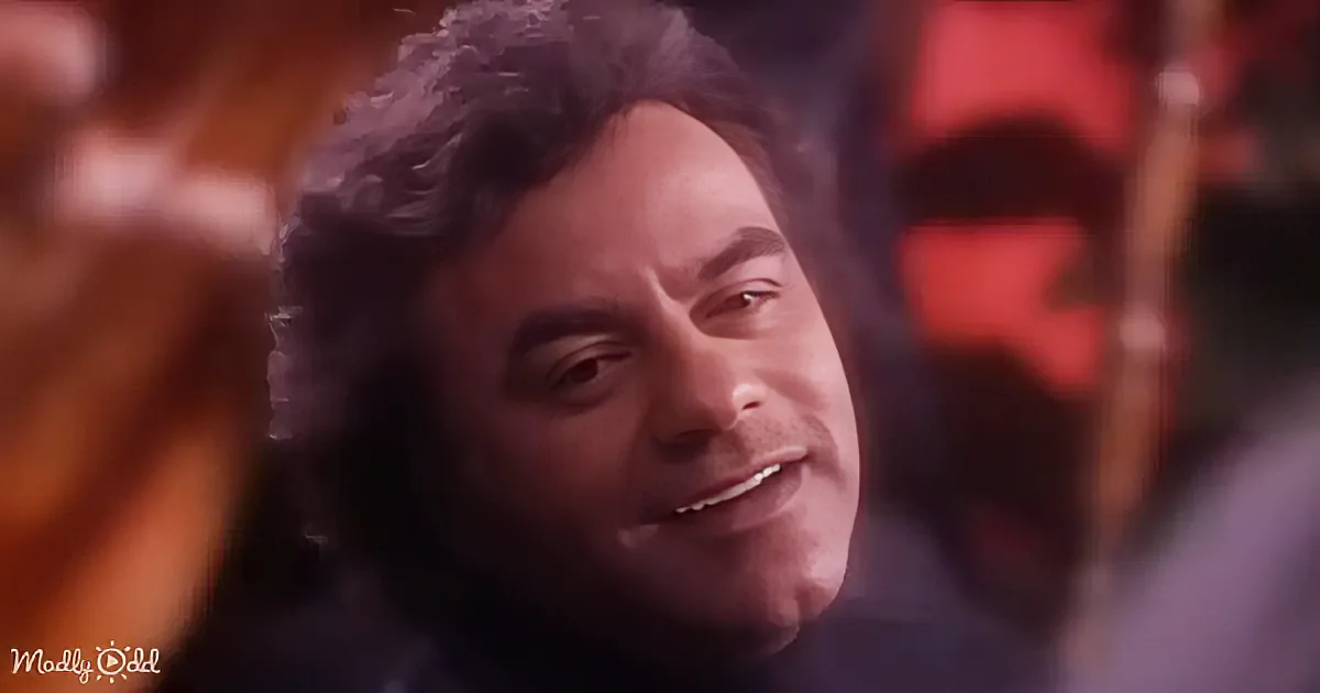 A person with curly hair and a dark outfit is shown in a close-up, smiling slightly.