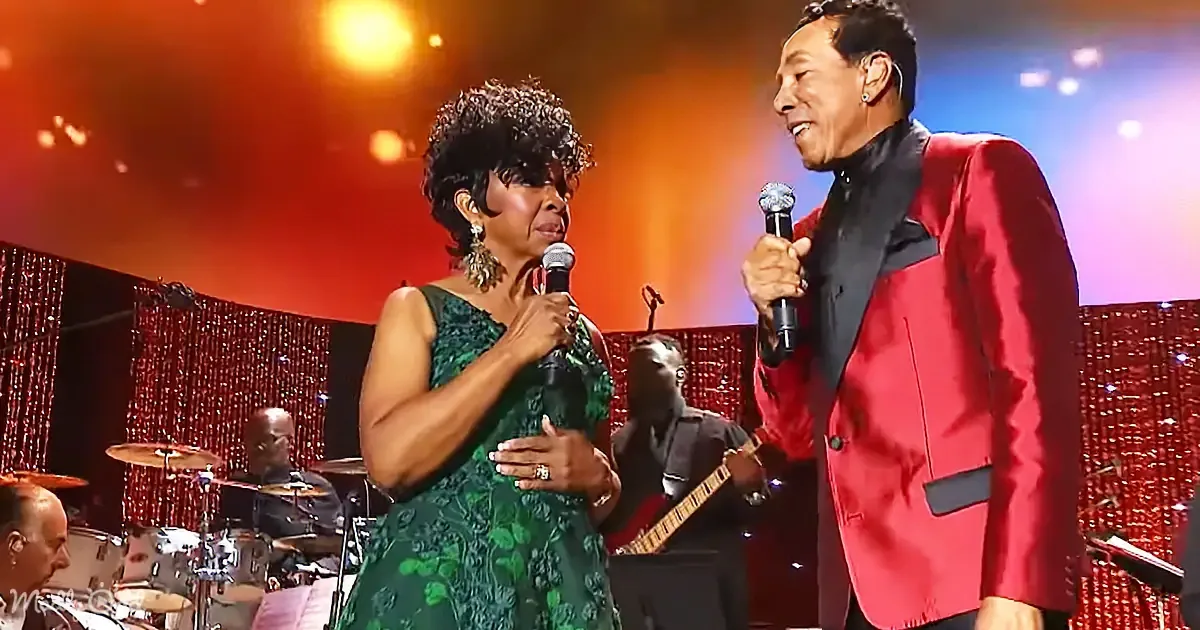 A woman in a green dress and a man in a red suit sing on stage with a band in the background.