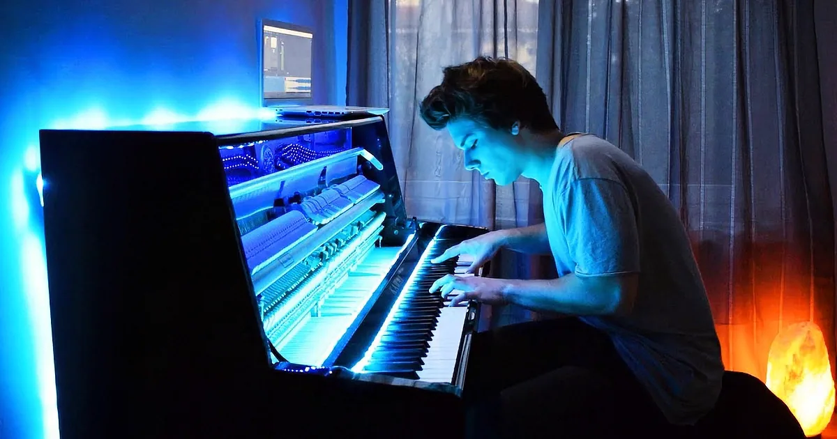 A person plays a piano illuminated by blue light, with a warm fireplace in the background.