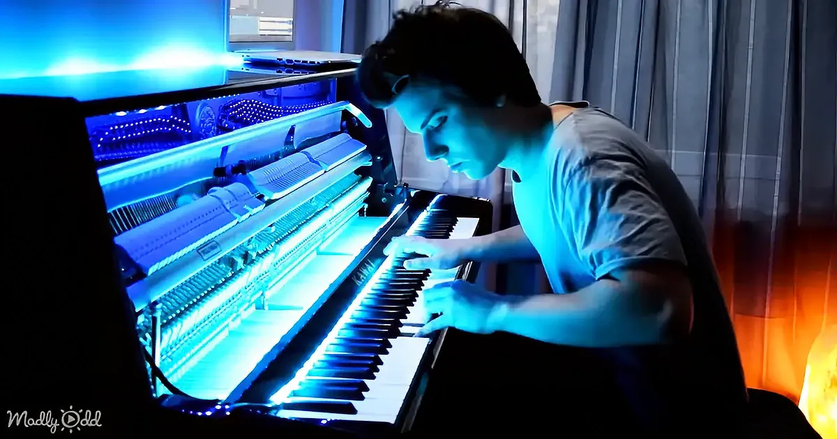 A person plays a piano illuminated by blue light, with a computer setup in the background.