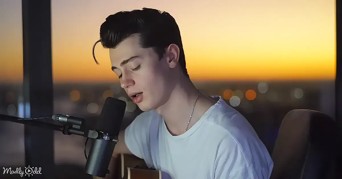 A person singing into a microphone, wearing a white shirt, with a cityscape and sunset in the background.