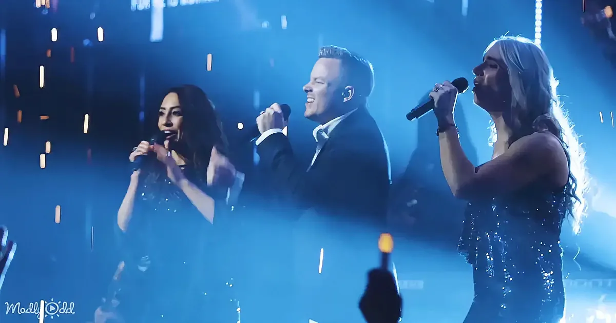 A group of performers singing on stage with microphones, illuminated by blue lights and sparkles.