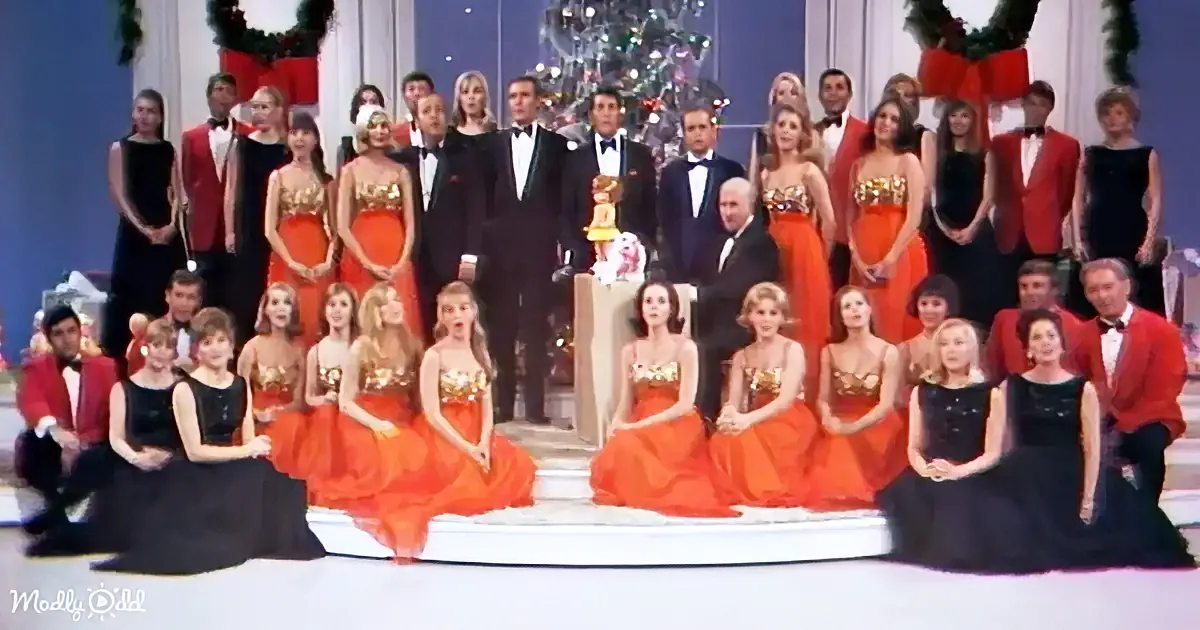 A group of people in formal attire, including red and black dresses and tuxedos, posing for a photo in front of a...
