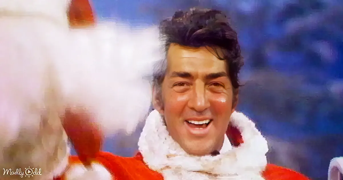 A smiling man in a red outfit with a white scarf, holding a red object, with a blurred background.