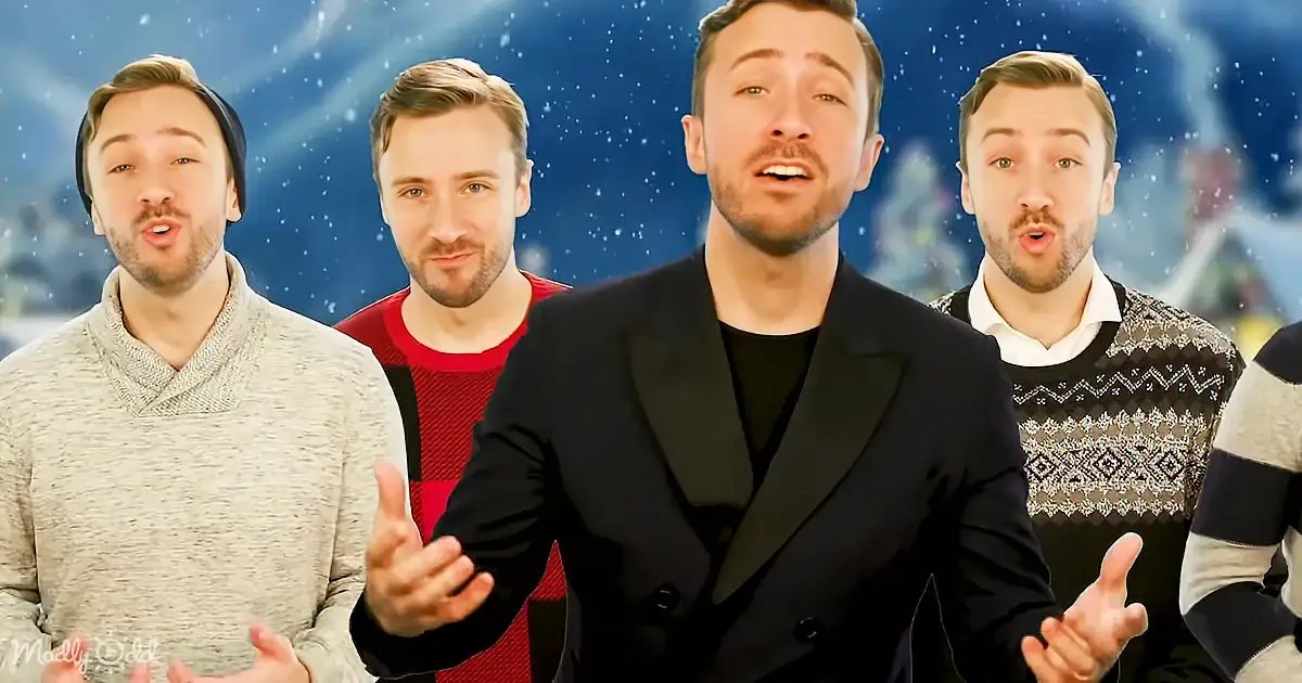 A man in a black suit gestures while four others in sweaters stand behind him against a snowy background.