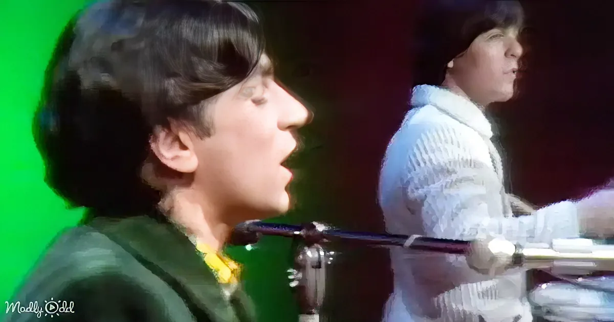 A person in a green jacket sings into a microphone, with another person in a white shirt in the background.