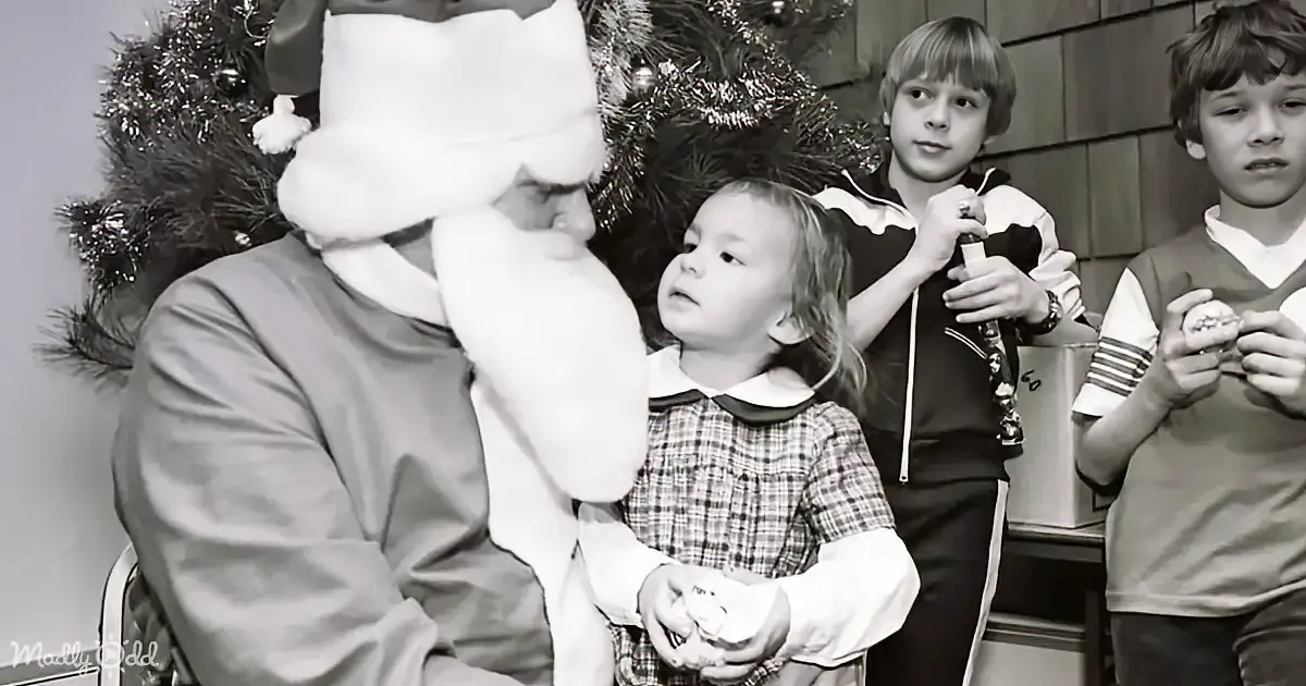 Children hold toys and a Lego set in front of a decorated Christmas tree.