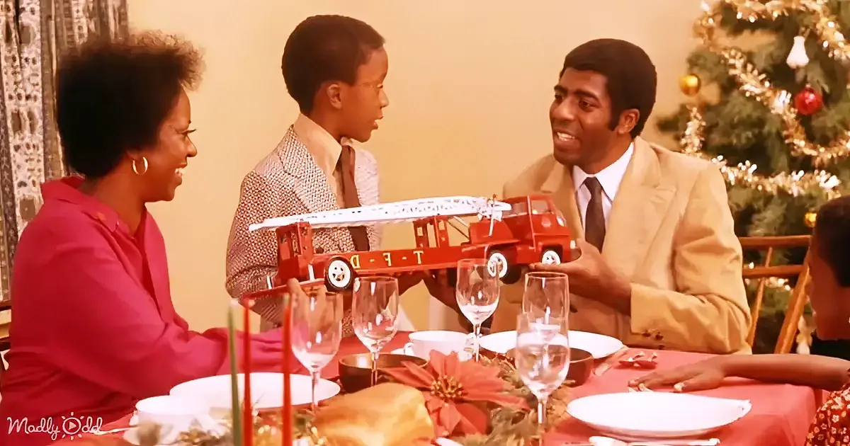 A family celebrates Christmas at a table with a toy fire truck, surrounded by festive decorations.