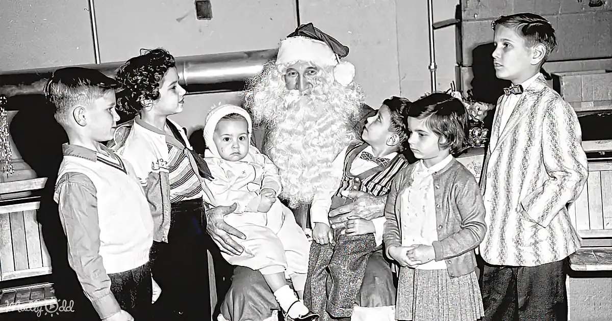 Santa Claus holds a baby surrounded by children in a vintage setting.