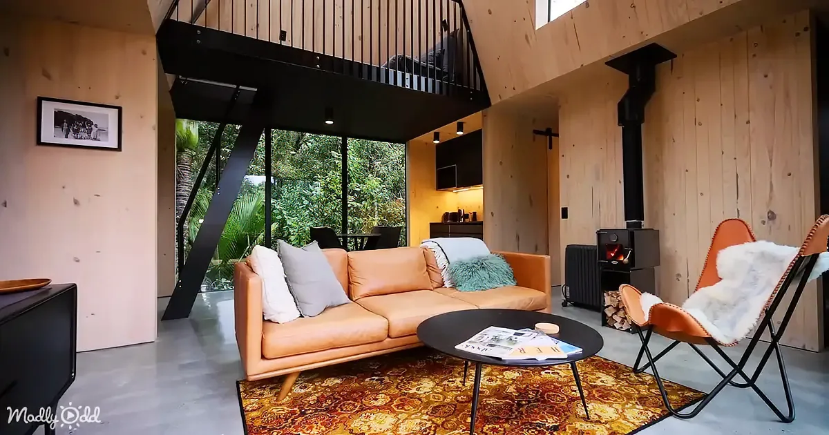 A cozy living room with a tan leather sofa, a black coffee table, and a fireplace, surrounded by wooden walls and a glass...