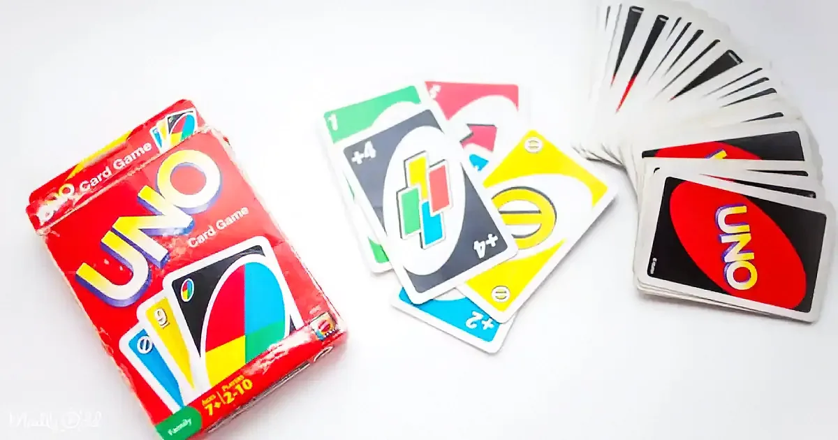 Uno card game box and scattered cards with colorful symbols on a white surface.