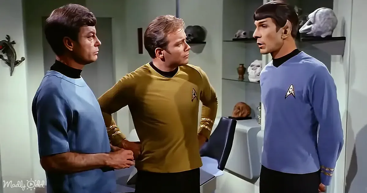 Three Star Trek characters in a room, one in yellow, two in blue, discussing something.