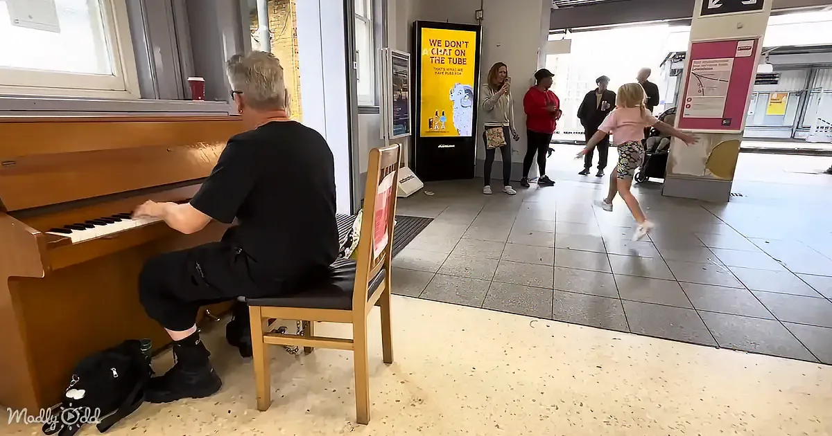 A man plays a piano while a girl dances nearby in a public space.