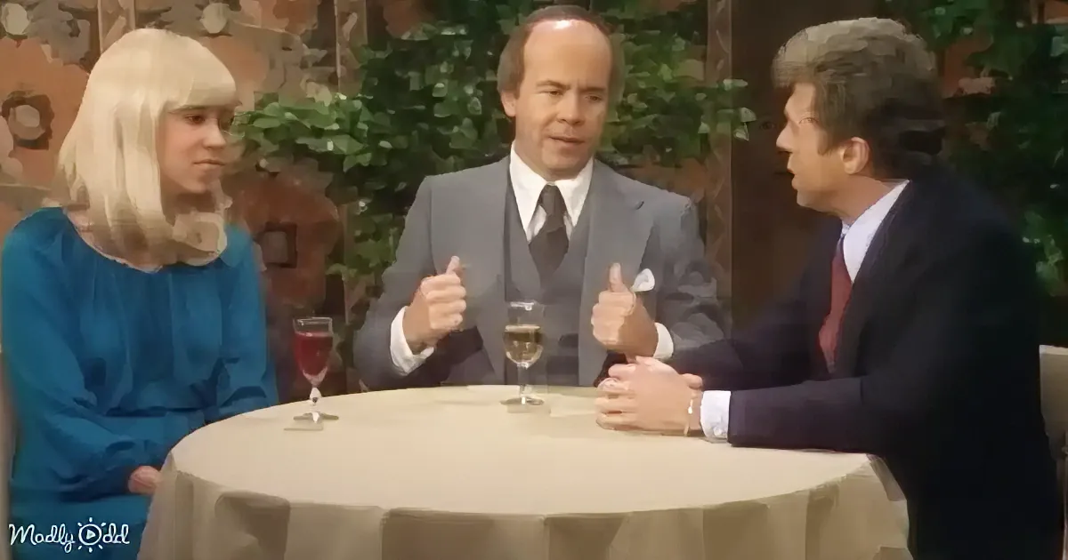 Three people in formal attire sit at a table with drinks, engaged in conversation.