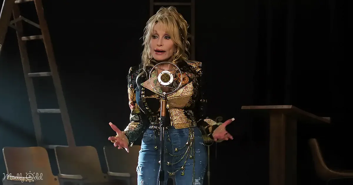 A person in a colorful, patterned outfit stands on stage, gesturing near a microphone.