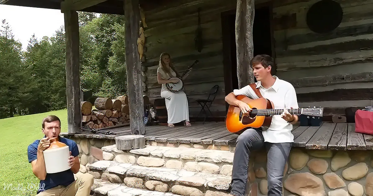A man plays guitar on a porch, another holds a jug, a woman plays banjo in the background.