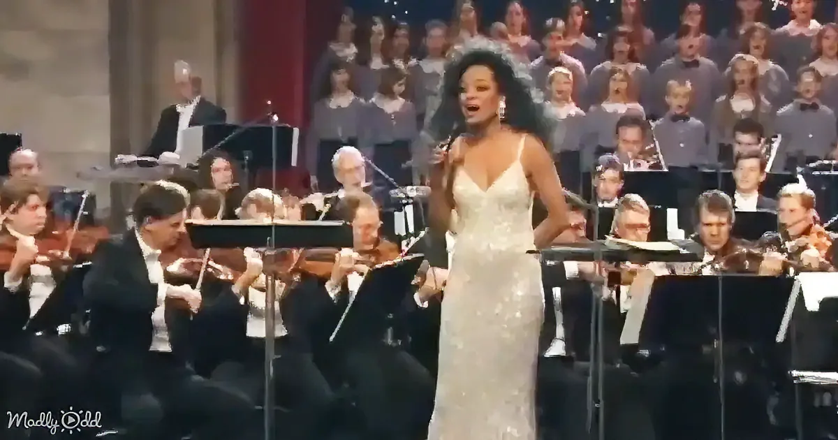 A woman in a white dress sings passionately in front of an orchestra and choir.