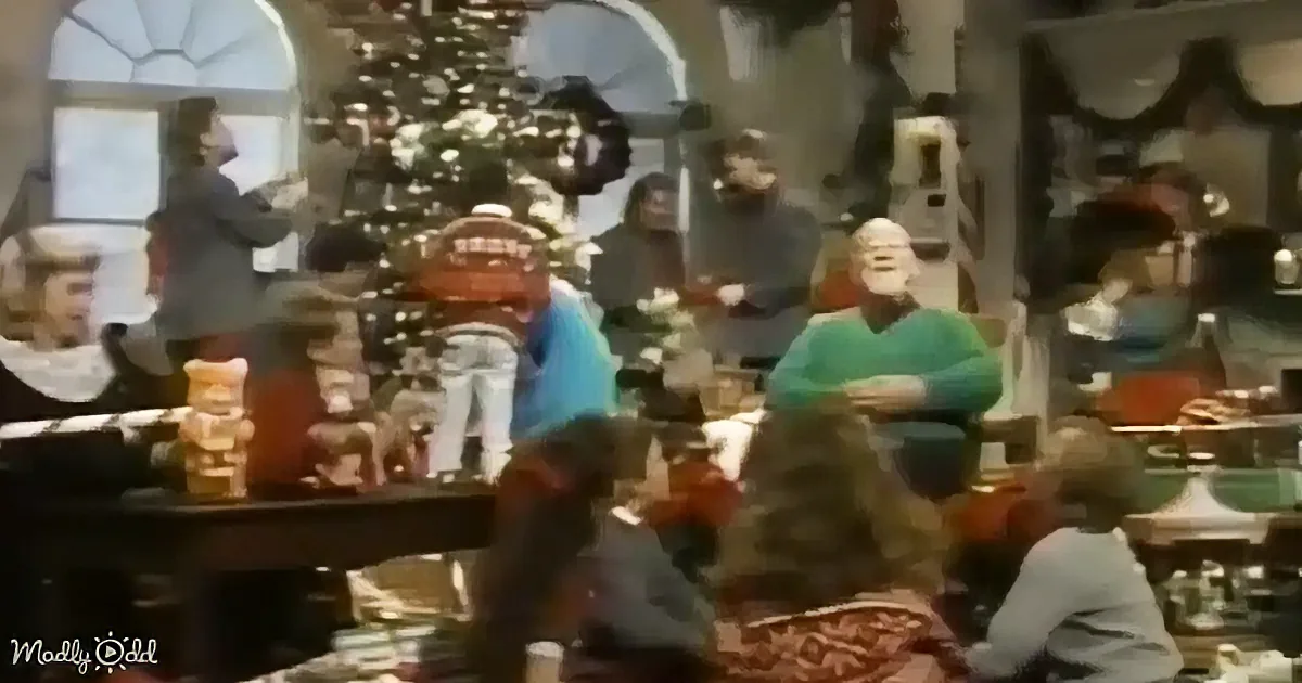 A man in a green sweater stands in a festive room with a Christmas tree and people around.