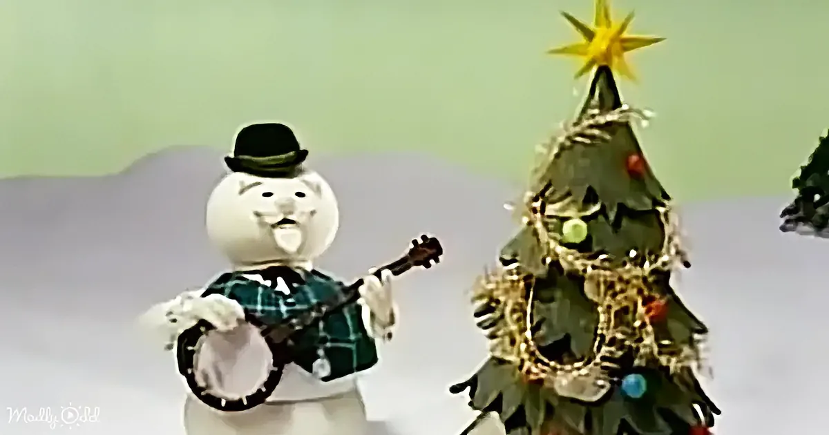 A snowman in a hat plays a banjo next to a decorated Christmas tree with a star on top.