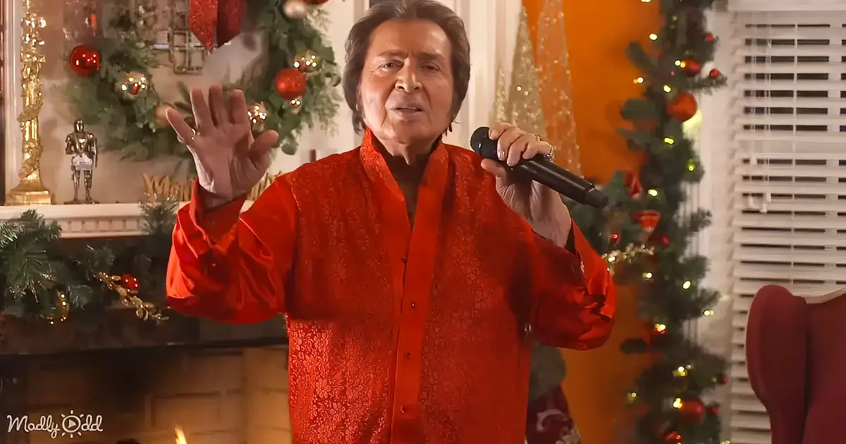 A person in a red patterned shirt sings into a microphone, surrounded by Christmas decorations.