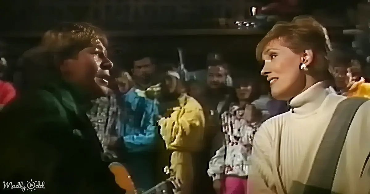 A man in a green jacket and a woman in a white turtleneck are facing each other, surrounded by a crowd.