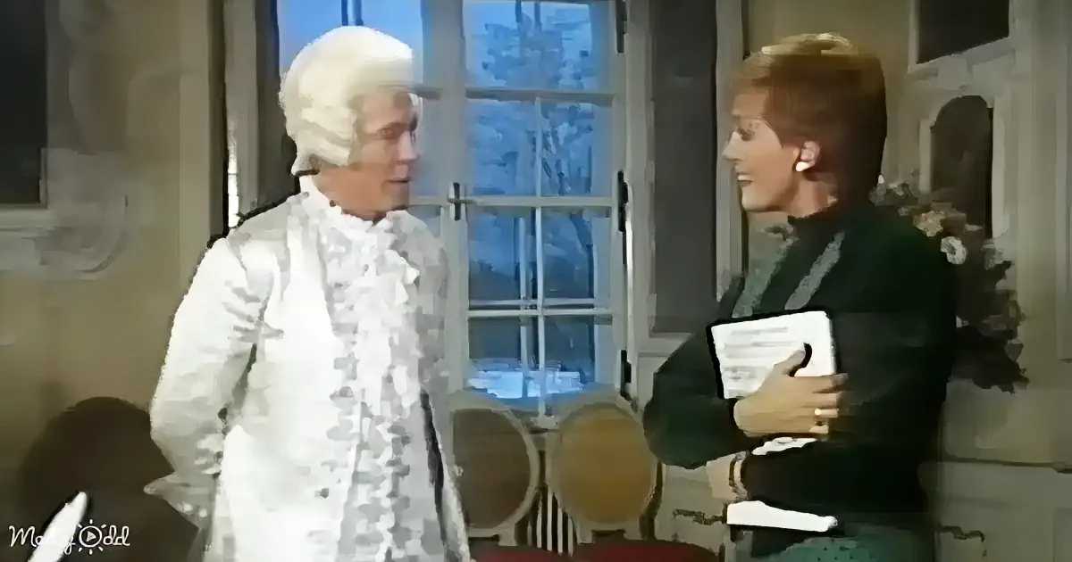 A man in a white historical costume stands next to a woman holding a book, both in a room with large windows.