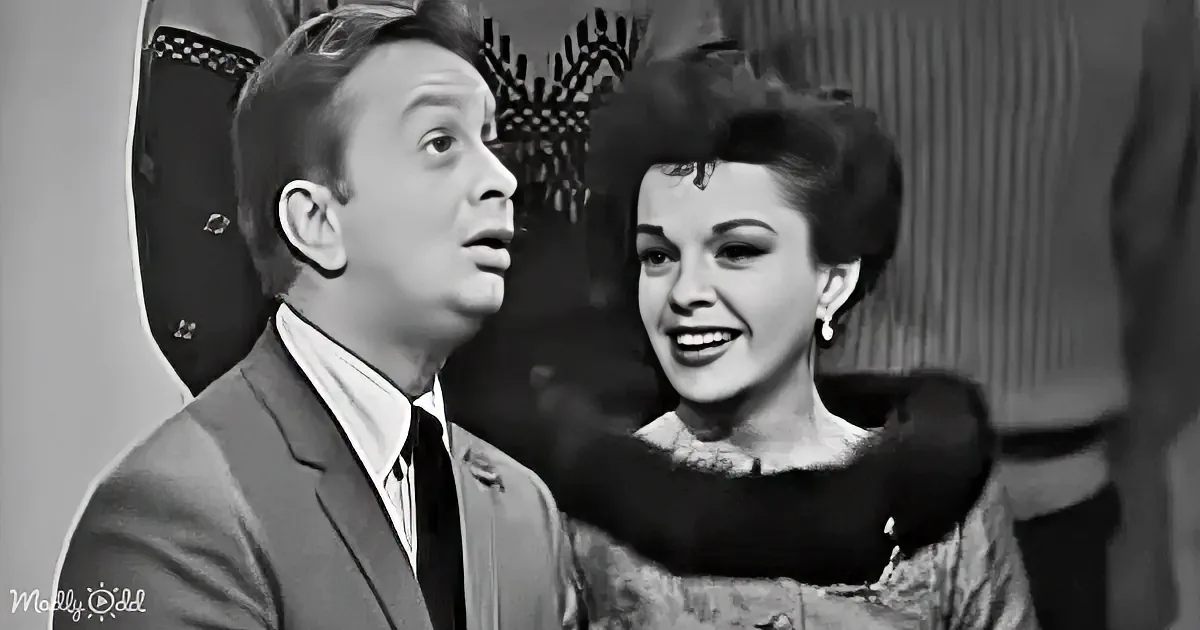 A man in a suit and a woman in a fur-trimmed dress are interacting, with the woman smiling and the man looking up.