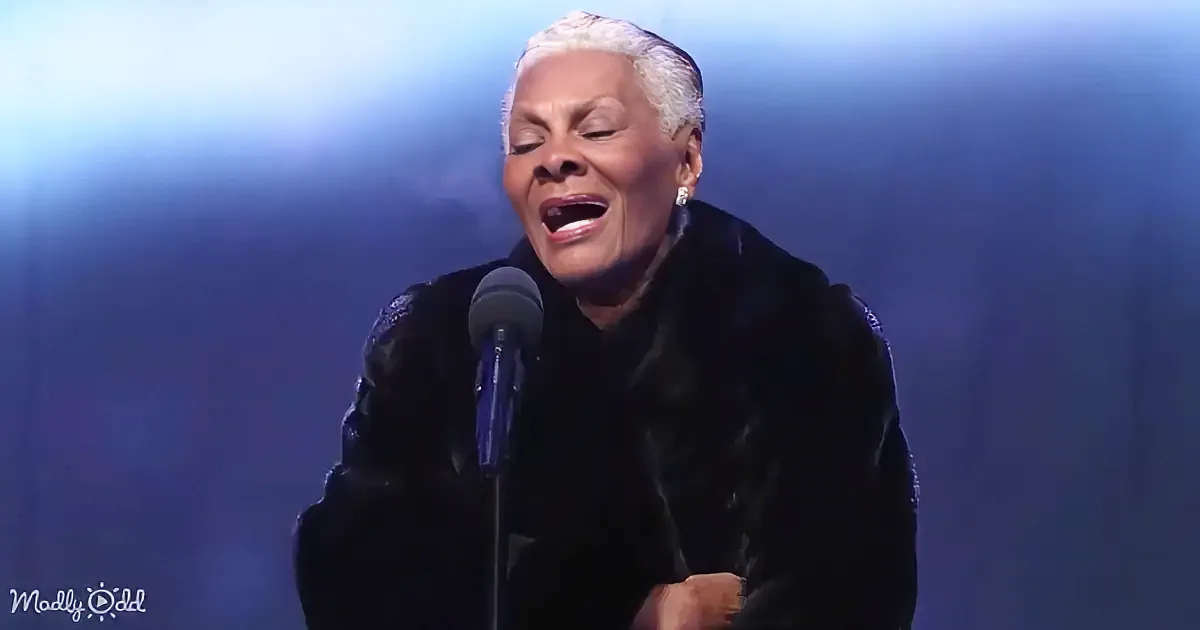 A woman in a black outfit sings passionately into a microphone on stage.