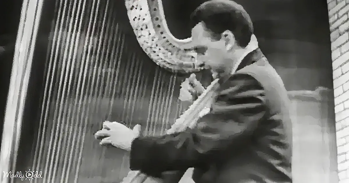 A man in a suit plays a harp, focusing intently on the instrument.