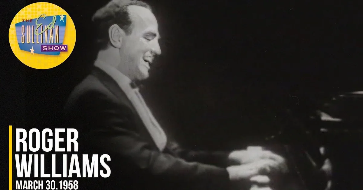 A man in a suit and bow tie smiles at the camera, seated at a piano.