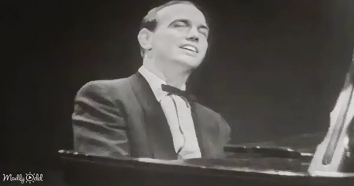 A man in a suit and bow tie sings passionately at a piano, with another person partially visible.