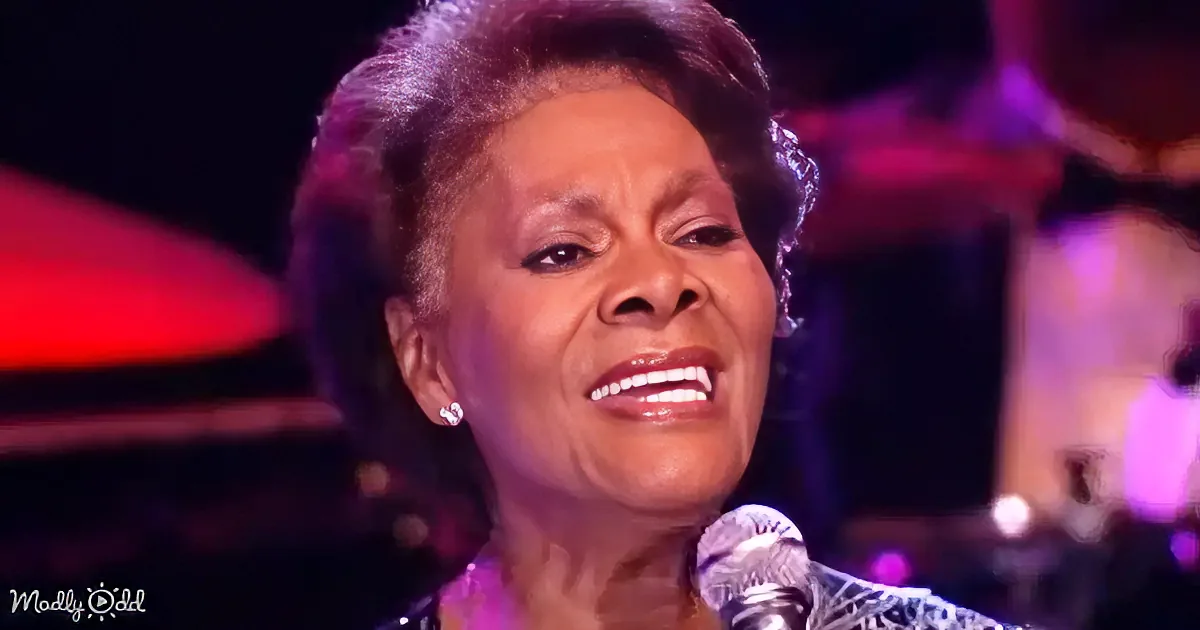 A woman with short hair and earrings smiles while singing into a microphone.