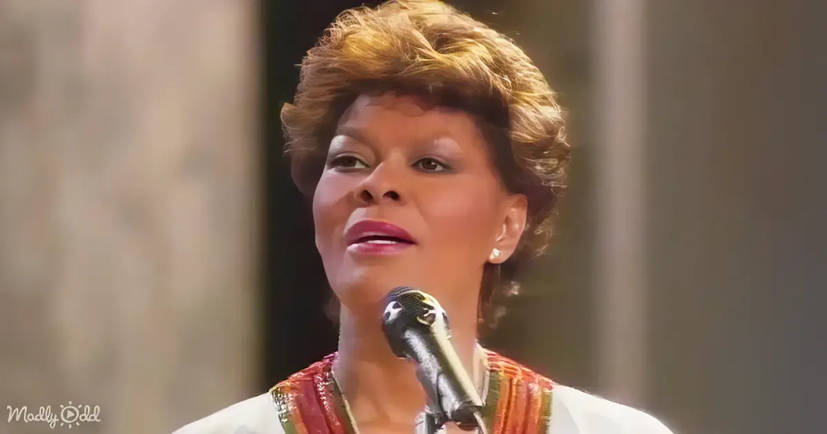 A woman with short, styled hair and a colorful outfit is speaking into a microphone.