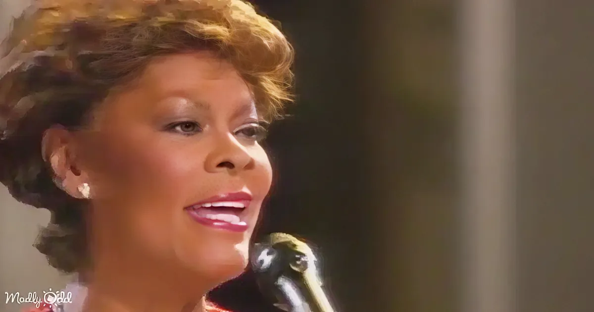 A woman with styled hair and earrings is singing into a microphone.