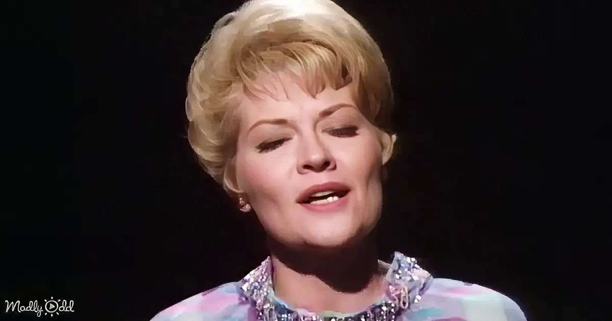 A woman with short blonde hair and a colorful outfit is singing on stage.