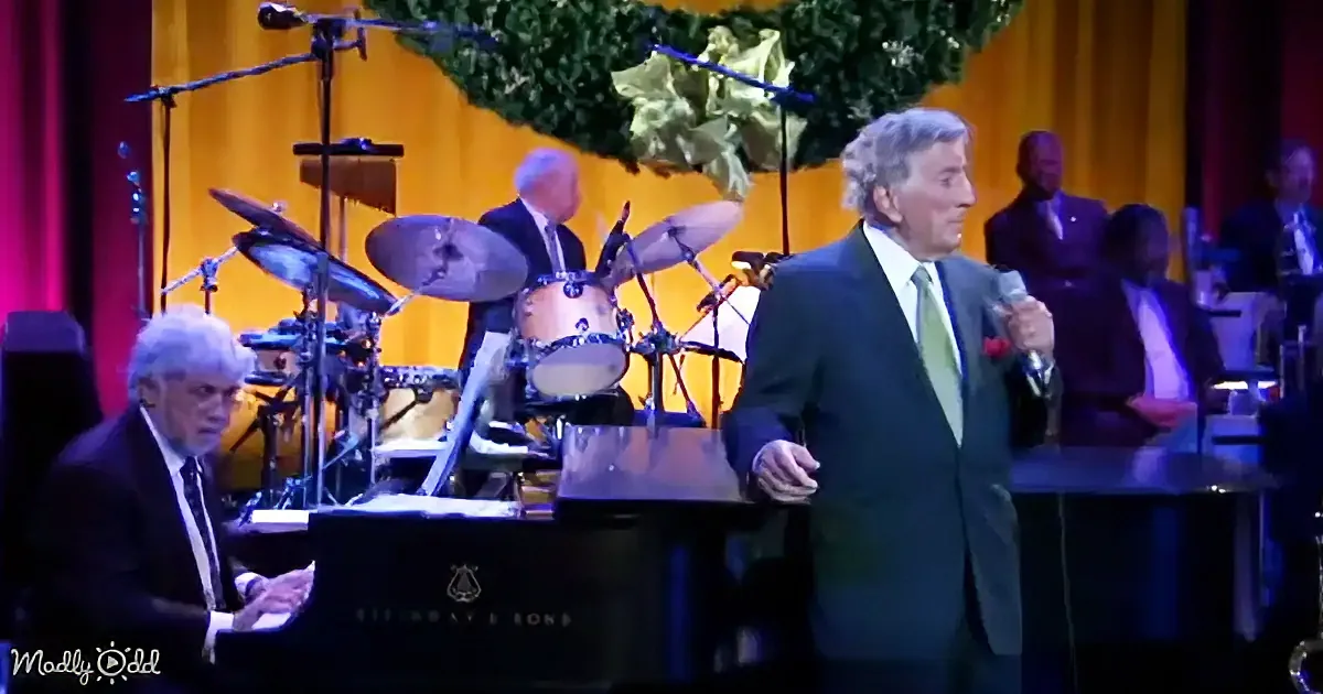 A man in a suit sings into a microphone while another plays piano in a vibrant stage setting.