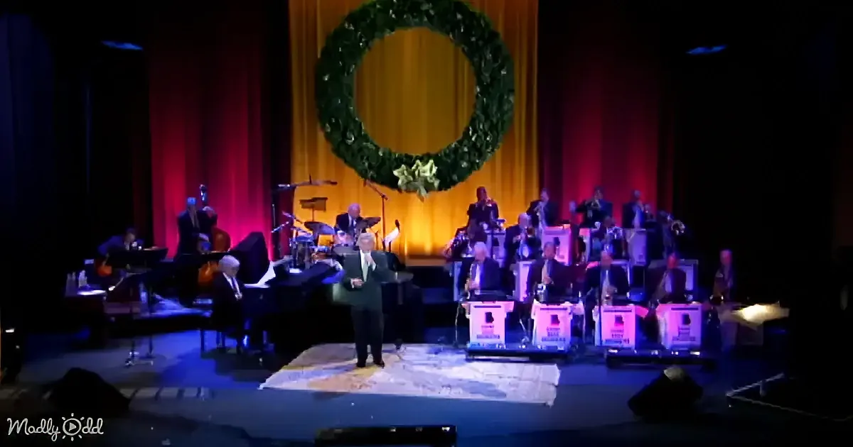 A conductor leads a band on stage with a large wreath backdrop.