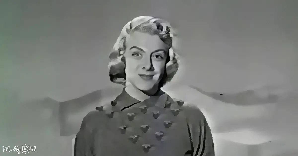 A woman with short, styled hair and a patterned top stands against a blurred background.