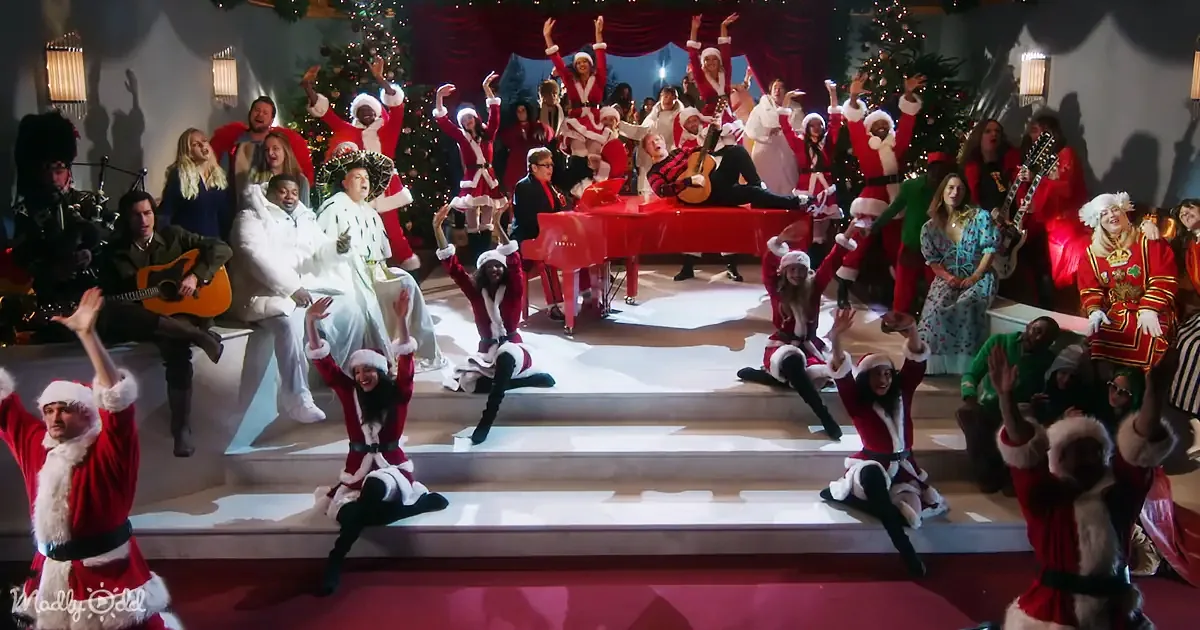 A group of people in festive attire, including Santa costumes, are joyfully performing on a stage.