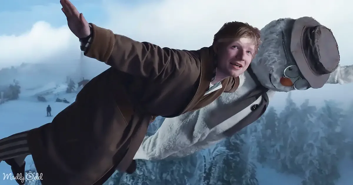 A person in a brown coat is flying through the air with a snowman, set against a snowy landscape.