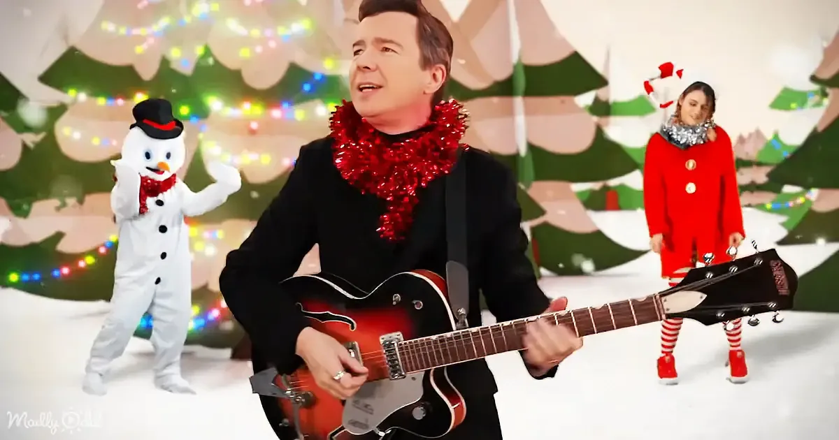 A man in a black suit plays a red guitar, adorned with a red tinsel scarf, in a festive Christmas setting.