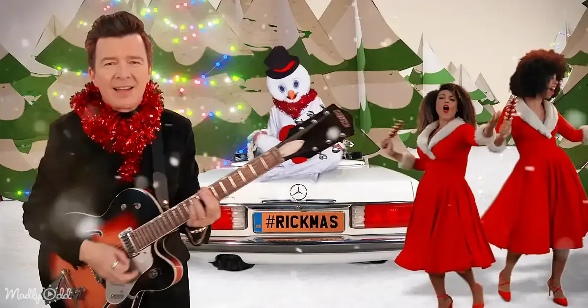 A man in a black suit plays guitar in a festive Christmas scene with a snowman and two women in red dresses.