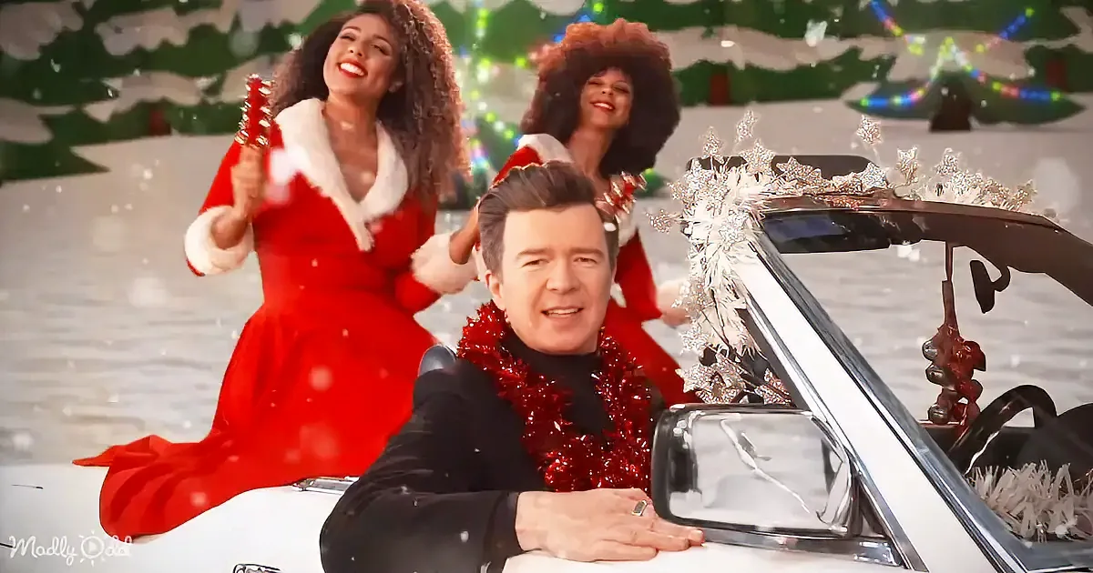A man in a black suit with red tinsel around his neck sits in a white car decorated with Christmas ornaments.