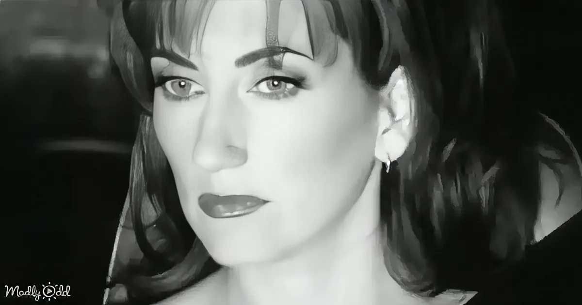 A woman with short hair and a black-and-white filter is holding a glass, looking to the side.