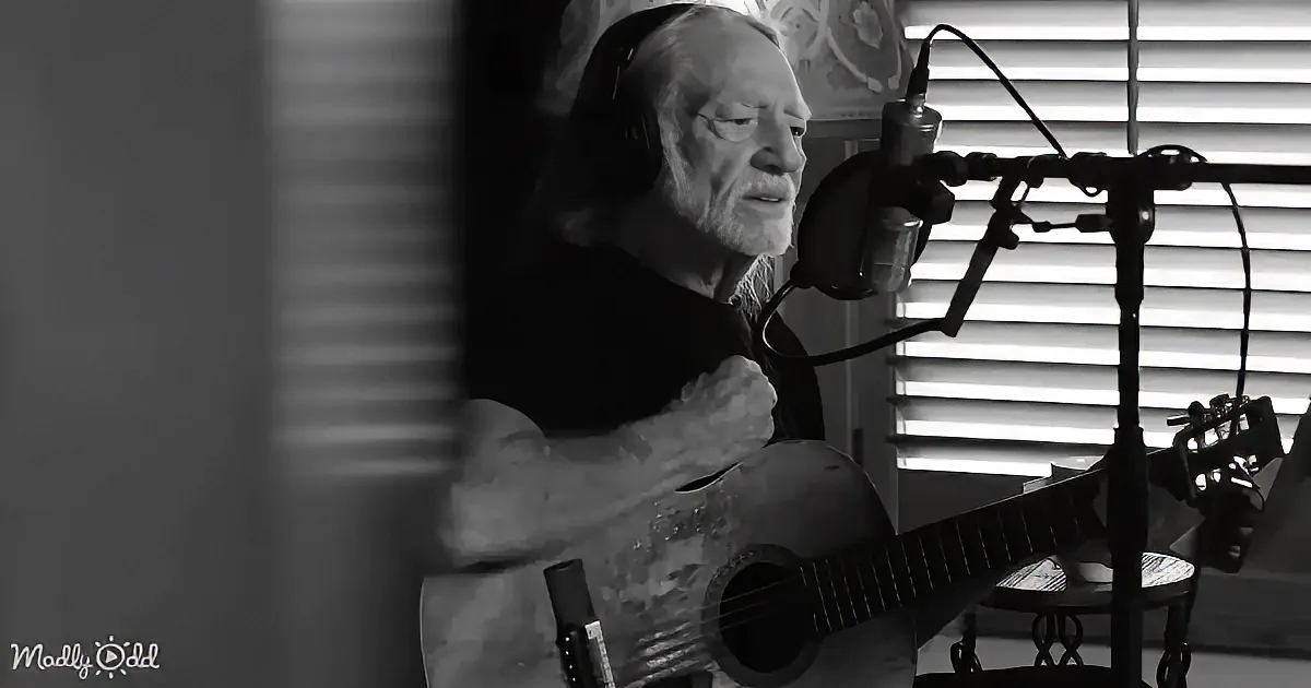 An older man with headphones sings into a microphone while playing an acoustic guitar.