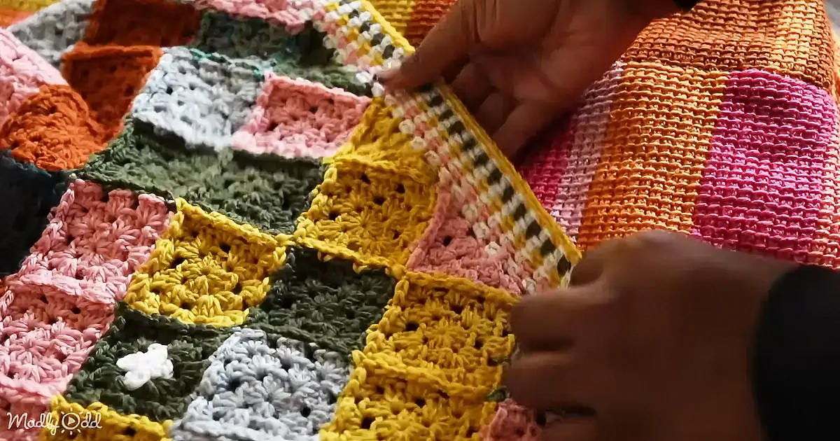 A person's hands are working on a colorful crocheted blanket with hexagonal patterns.