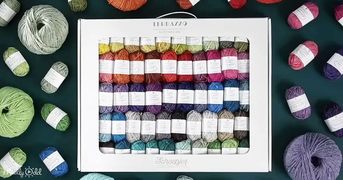 A box of Ferrazzo yarns in various colors is surrounded by scattered yarn balls on a dark green surface.